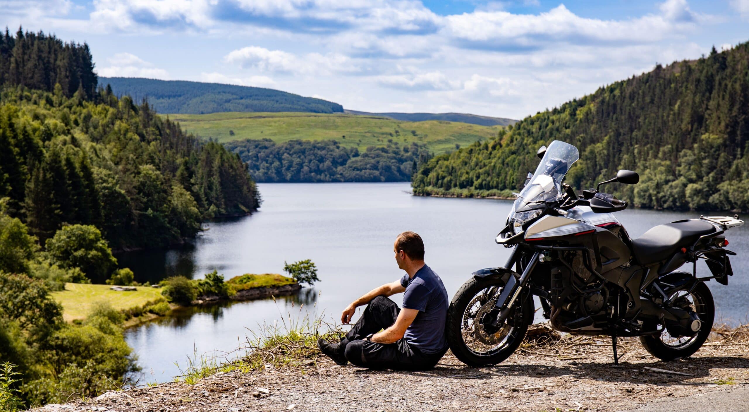 Honda NT-1100 DCT Zubehör im Toureneinsatz: Tourenfahrer entspannt am See neben Reise-Motorrad mit Windschild und vollständiger Ausstattung